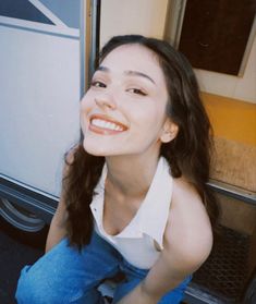 a young woman sitting on the floor next to a bus and smiling at the camera