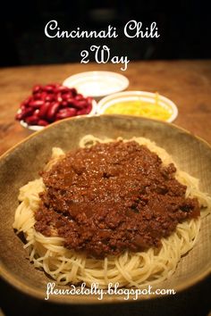 a bowl filled with spaghetti and sauce on top of a wooden table next to bowls of beans