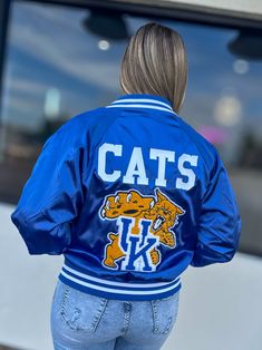 Get ready to show off your school spirit in style with our Kentucky Bomber Jacket! This cute and sporty jacket features a royal blue color and a Kentucky design, making it perfect for game days or any day. Stay warm and look amazing with this must-have addition to your wardrobe. Go Wildcats! Unisex sizing + fit Adult Small - 3XL SPECIAL CARE - WASHING INSTRUCTIONS: Hand washing and air drying are always best for these items. Wash on delicate, cold, and inside out. Always air dry to prevent lint Team-colored Outerwear With Team Name For Game Day, Team-colored Outerwear With Team Name For Sports Season, Team Outerwear For Game Day, Game Day Long Sleeve Varsity Jacket With Team Name, Team-colored Outerwear For Game Day With Team Spirit, Varsity Jacket With Team Name For Game Day, Game Day Varsity Jacket With Team Name, Team-colored Outerwear For Game Day, Team Spirit Hooded Fall Outerwear