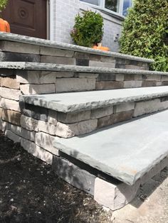 an outdoor stone wall with steps leading up to the front door and pumpkins in the background