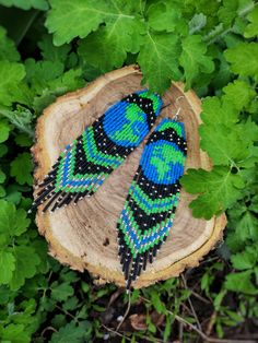 two blue and green beaded birds sitting on top of a piece of wood next to leaves