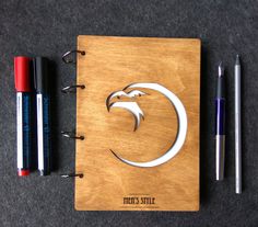 a wooden notebook with an eagle on the cover and two pens next to it,