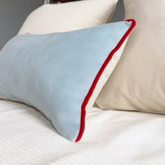 two pillows on top of a bed with white sheets and red piping around the edges