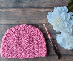 a pink crocheted hat next to a white flower and a pair of scissors