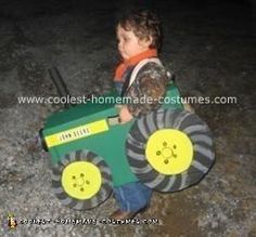 a little boy in a costume holding a toy tractor and steering wheel on the ground