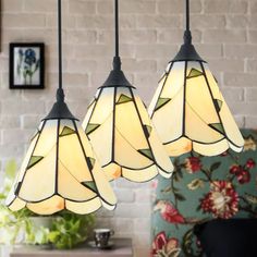 three lights hanging from a ceiling in a room with a brick wall and chair behind them