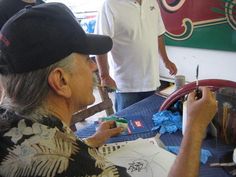 an older man is drawing on paper while two other men stand in the background