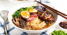 a bowl filled with noodles, meat and vegetables next to chopsticks on a table