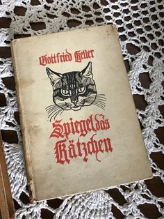 an old book with a cat's face on it sitting on a doily