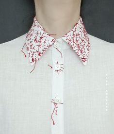 a close up of a person wearing a white shirt with red designs on the collar