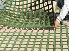 a man kneeling down next to a green grass covered area with bricks and cement blocks