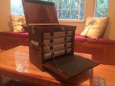 an open briefcase sitting on top of a wooden table in front of a window with pillows