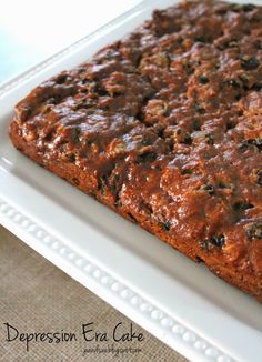 a close up of a square cake on a white plate with a brown table cloth