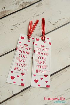 two bookmarks with red and white hearts are sitting on a wooden surface, one has a ribbon around it