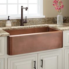 a large copper sink in a kitchen with marble counter tops and white cabinets, along with pink flowers