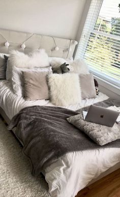 a bed with pillows, blankets and a laptop on top of it in front of a window