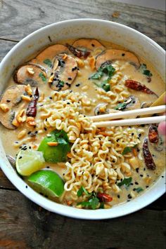 a bowl filled with noodles and vegetables next to chopsticks on a wooden table