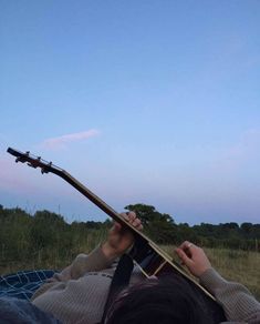 a person laying down with a guitar in their lap and looking up at the sky