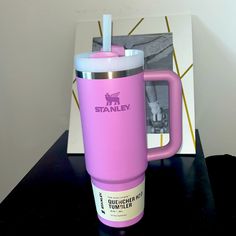 a pink coffee mug sitting on top of a black table next to a photo frame