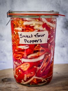 a jar filled with lots of red and white peppers sitting on top of a wooden table