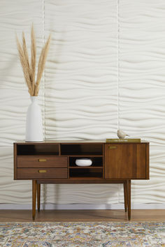 a white vase sitting on top of a wooden table next to a brown cabinet with drawers