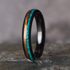 a wedding band with blue and green inlays on top of a stone slab