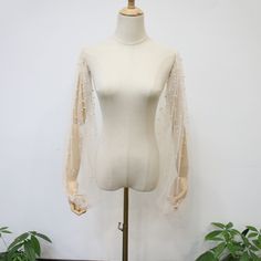 a white mannequin with sheer sleeves on it's head and neck, next to potted plants