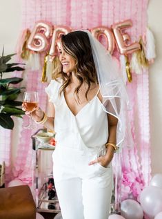 a woman holding a glass of wine in front of a balloon wall with the word bride on it