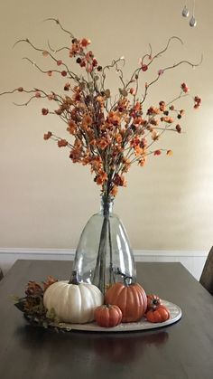 an arrangement of pumpkins and flowers in a vase on a table with a plate