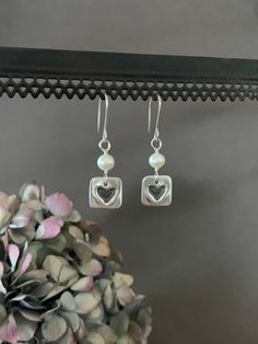 "White Pearl Earrings, Square Sterling Silver and Fresh Water Pearl Dangle Earrings, Heart Earrings, Bridesmaid Gift, Bride, Wedding Gift Simple but, elegant earrings. They are adorned with sterling silver heart charms and fresh water pearls.  Lightweight and versatile. Perfect for everyday and would be beautiful on a bride, gift for bridesmaid or mother of bride.  Pearls are known as the \"stone of sincerity\", it signifies faith, and purity. They are said to help with fertility and work as a calming stone by getting rid of negative energy. Fresh Water Pearls are also known for promoting sincerity truth, and loyalty.  We use only fine and sterling silver for all of our jewelry and findings, including our handmade earwires. Our unique hand forged metalwork is shaped and hammered for simpli Silver Pearl Earrings For Valentine's Day, Dangle Earrings For Anniversary And Mother's Day, Silver Heart-shaped Pearl Earrings For Valentine's Day, Valentine's Day Dangle Pearl Earrings For Pierced Ears, Silver Heart Earrings With Pearl Drop, Handmade Silver Earrings For Bridesmaid Gift, Wedding Double Heart Earrings, Heart-shaped Wedding Earrings, Heart Cut Pierced Earrings For Wedding