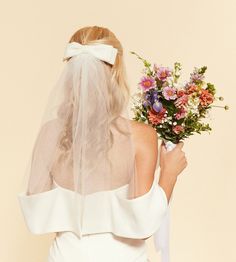 the back of a bride's dress with a veil on her head and flowers in her bouquet