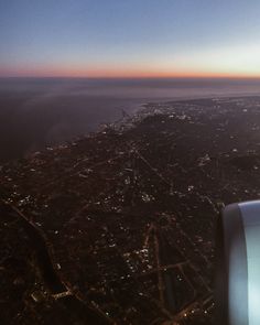 an airplane wing flying over a city at night with the sun setting in the distance