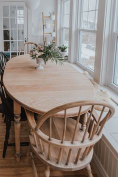 a wooden table with chairs around it in the middle of a room filled with windows