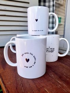 three white coffee mugs sitting on top of a wooden table next to a window