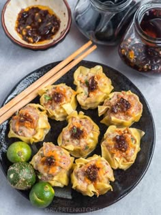 some dumplings are on a black plate with chopsticks next to them and sauce