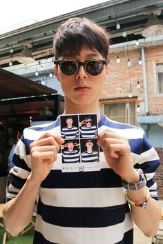 a young man wearing sunglasses and holding up a card with photos on it in front of him