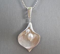 A lovely Calla Lily pendant in brushed silver has double lustrous white Freshwater pearls in its center. It hangs simply from a delicate silver ball chain. Length measures 16 inches but can easily be adjusted upon request.  A perfect necklace for bridesmaids or bridal parties!  Pendant measures almost 1 1/2 inches in length and 1 inch in width. Delicate Silver Teardrop Pearl Necklace, Sterling Silver Drop Necklace With Pearl Pendant For Wedding, Wedding Pearl Drop Flower Pendant Necklaces, Delicate Silver Drop Necklace For Anniversary, Wedding Pearl Drop Flower Pendant Necklace, Wedding Pearl Necklace With Flower Pendant, Silver Drop Necklace With Pearl Pendant For Anniversary, Silver Pearl Wedding Necklace With Flower Pendant, Silver Teardrop Pearl Necklace For Anniversary