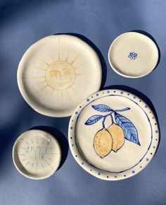 three plates with designs on them sitting on a blue tablecloth, one has lemons and the other has leaves