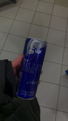 a person holding a can of blue bull energy drink in their left hand, on a tiled floor