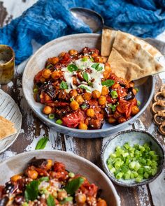 two bowls filled with food next to some pita bread and green onions on a wooden table