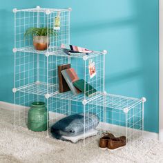 three tiered shelving unit with books and other items on the floor in front of a blue wall