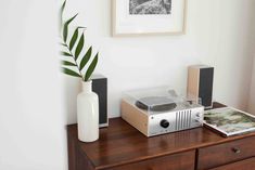 a record player sitting on top of a wooden table next to a vase with a plant