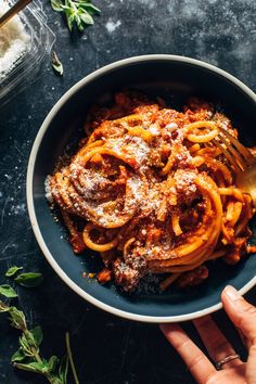 a bowl filled with pasta and sauce on top of a table next to some herbs