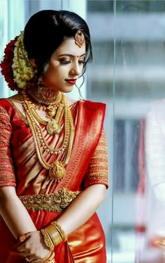 a woman in an orange and red sari with gold jewelry on her neck is looking at the camera