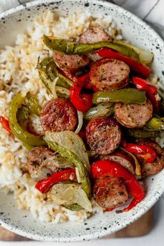 a white bowl filled with sausage and peppers on top of rice covered in gravy