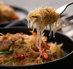 a spoon full of noodles and vegetables being lifted from a skillet with chopsticks