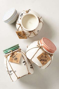 three small jars with labels on them are sitting next to each other and one has a candle in it