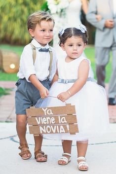 two young children dressed up in formal clothes and holding a sign that says ya viene la noivaa