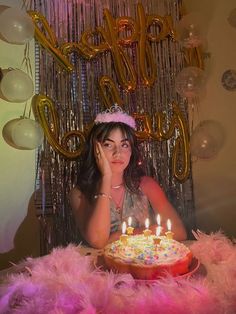 a woman sitting in front of a birthday cake with lit candles on top of it