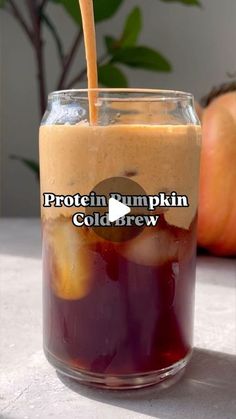 a glass filled with liquid sitting on top of a table next to two pumpkins